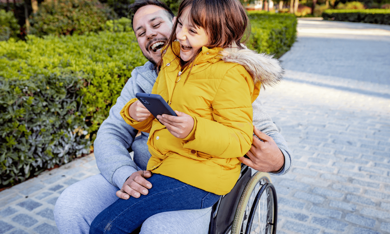 A Man laughing in a wheelchair with a little girl sitting on his lap.